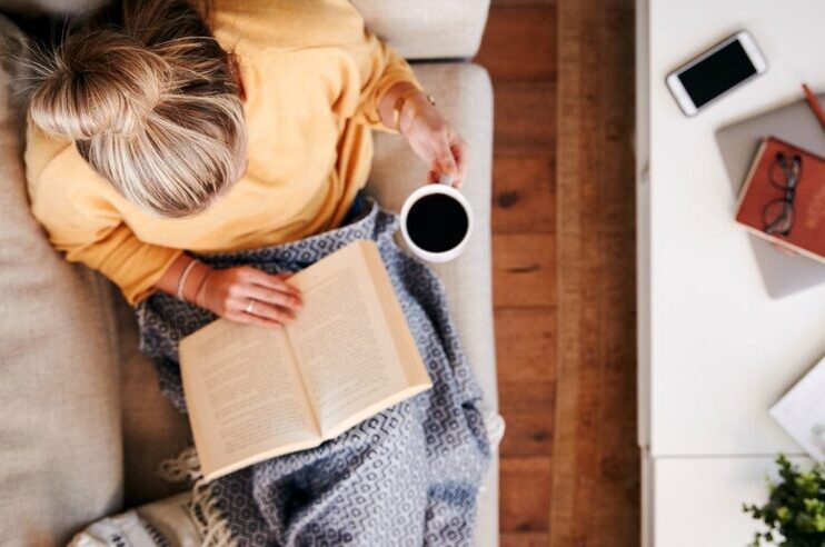 Uma senhora a ler um livro e a beber café