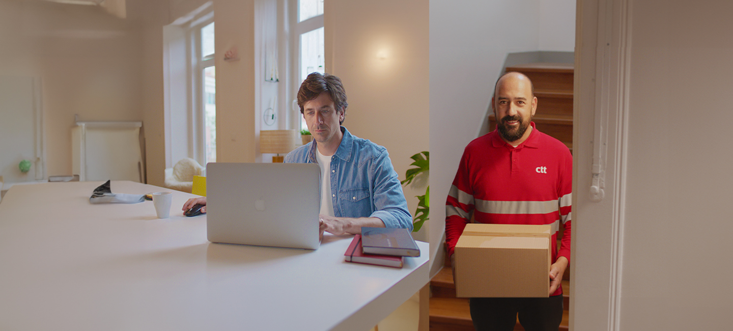 Duas pessoas numa sala, uma está sentada ao computador com livros e papéis, outra está com a farda dos CTT e com uma encomenda na mão.