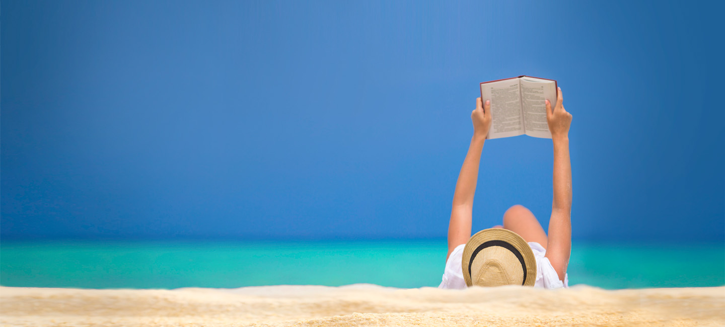Senhora deitada na areia da praia a ler um livro.