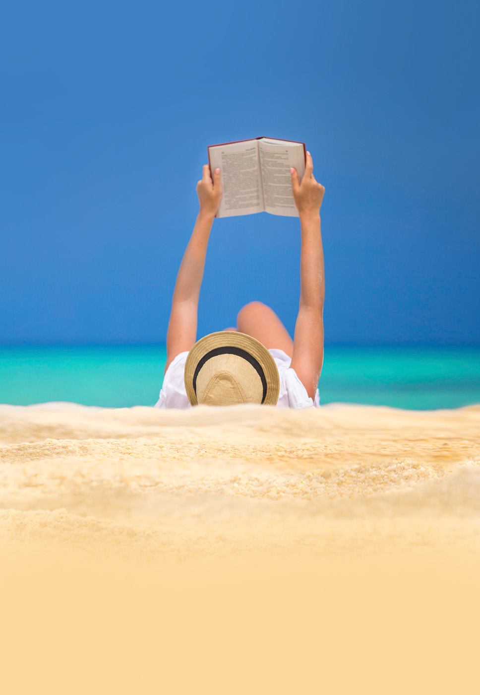 Senhora deitada na areia da praia a ler um livro.